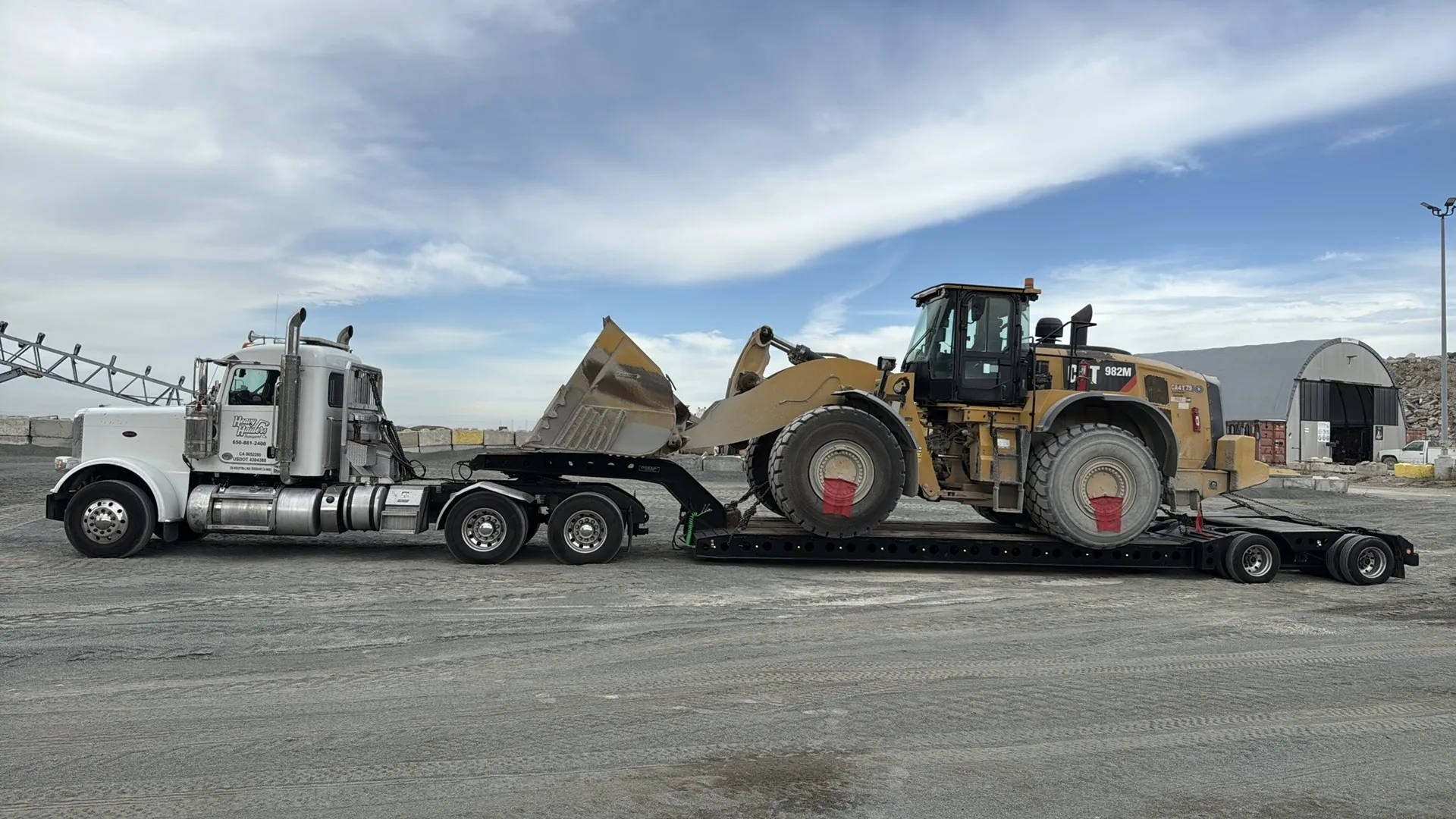 Heavy Haulers white Peterbilt lowboy hauling a CAT 982M wheel loader under a clear California sky